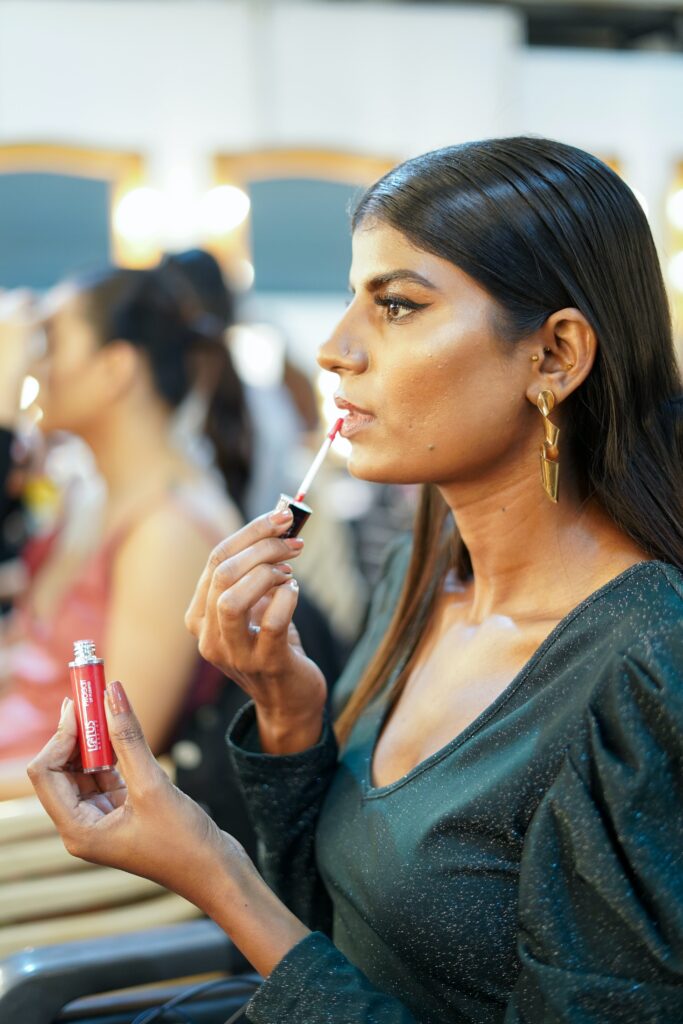 Trendy model applying lip gloss in dressing room
