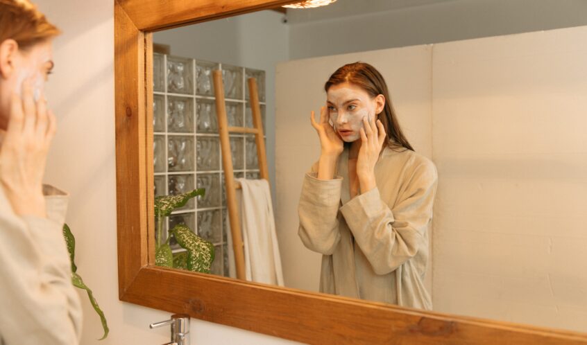 Person Applying Cosmetic Product on Her Face While Looking at the Mirror